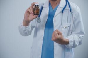 Portrait of young Asian male doctor smiling, showing a Medicine bottle and looking by Confident while standing Friendly and kind in the hospital. Healthcare and medical insurance concept. photo