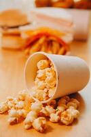 A bucket of popcorn, top-view, warm colors, light brown wooden background, flat lay, daylight macro close-up photo