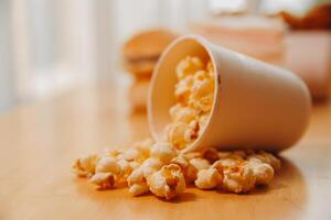 A bucket of popcorn, top-view, warm colors, light brown wooden background, flat lay, daylight macro close-up photo