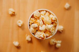 A bucket of popcorn, top-view, warm colors, light brown wooden background, flat lay, daylight macro close-up photo