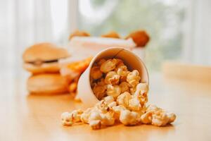 A bucket of popcorn, top-view, warm colors, light brown wooden background, flat lay, daylight macro close-up photo