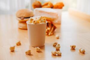 A bucket of popcorn, top-view, warm colors, light brown wooden background, flat lay, daylight macro close-up photo