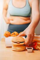 To eat or not. Cheerless plump woman looking at the burger while thinking to eat it or not photo