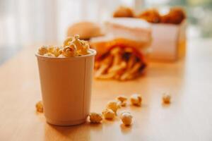 A bucket of popcorn, top-view, warm colors, light brown wooden background, flat lay, daylight macro close-up photo