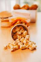 A bucket of popcorn, top-view, warm colors, light brown wooden background, flat lay, daylight macro close-up photo