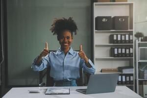 Happy excited successful Asian businesswoman triumphing with a laptop computer smartphone in the workplace office photo