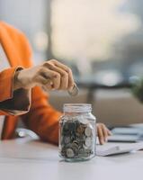 Beautiful Asian businesswoman insert coins in a pin piggy bank on the table. saving money, investment, currency concept photo