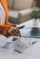 Beautiful Asian businesswoman insert coins in a pin piggy bank on the table. saving money, investment, currency concept photo