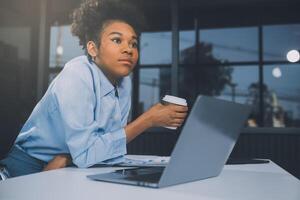 aburrido joven mujer en el oficina trabajando con un ordenador portátil y curioso a computadora pantalla foto