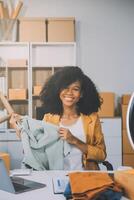 Moda blogger concepto, joven asiático mujer de venta ropa en streaming.startup pequeño negocio pequeño, utilizando teléfono inteligente o tableta tomando recibir y comprobación en oficina foto