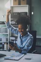 Happy excited successful Asian businesswoman triumphing with a laptop computer smartphone in the workplace office photo