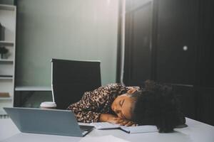 Young woman her head at office desk in front of laptop, feeling ruined, suffer from anxiety, about to attempt suicide, pregnancy, end of a working day, exhausted and unable to manage her emotions photo