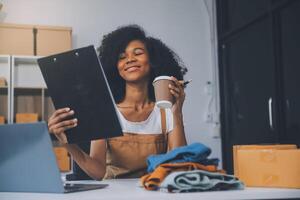 Startup SME small business entrepreneur of freelance Asian woman wearing apron using laptop and box to receive and review orders online to prepare to pack sell to customers, online sme business ideas. photo