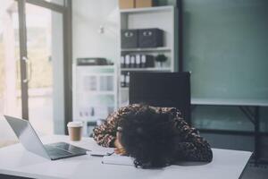 Young woman her head at office desk in front of laptop, feeling ruined, suffer from anxiety, about to attempt suicide, pregnancy, end of a working day, exhausted and unable to manage her emotions photo