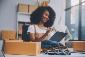 Startup SME small business entrepreneur of freelance Asian woman wearing apron using laptop and box to receive and review orders online to prepare to pack sell to customers, online sme business ideas. photo