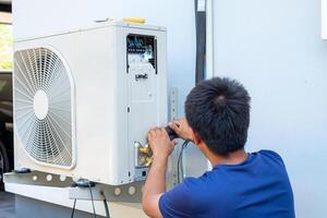 masculino técnico instalando al aire libre unidad de aire acondicionador a frio el casa en el verano. aire compresor, electrónico, caliente verano, alto temperatura, tropical países foto