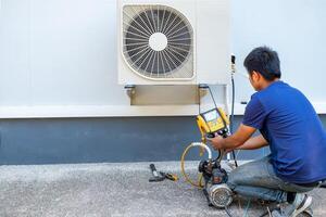 masculino técnico instalando al aire libre unidad de aire acondicionador a frio el casa en el verano. aire compresor, electrónico, caliente verano, alto temperatura, tropical países foto