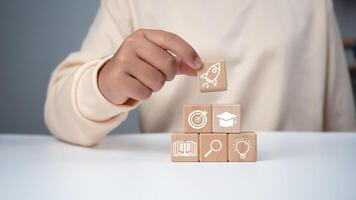 Man holding a wooden cube with printed educational symbols, E-learning education, internet lessons and online webinar. Education internet Technology. Success and necessary skills in graduation. photo