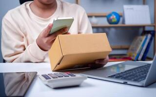 Woman runs an e-commerce business is checking orders from laptop, she owns an online store, she packs and ships through a private transport company. Online selling and online shopping concepts. photo