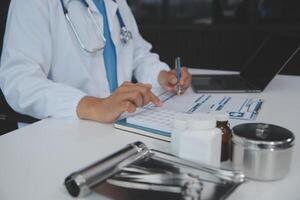 un profesional y enfocado asiático hembra médico en matorrales es trabajando y leyendo médico investigación en su ordenador portátil en su oficina a un hospital. foto