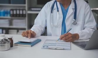 A professional and focused Asian female doctor in scrubs is working and reading medical research on her laptop in her office at a hospital. photo