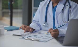 un profesional y enfocado asiático hembra médico en matorrales es trabajando y leyendo médico investigación en su ordenador portátil en su oficina a un hospital. foto