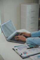 encantadora joven mujer de negocios asiática sentada en una computadora portátil en la oficina, haciendo un informe que calcula el documento de verificación del servicio de ingresos internos del saldo. foto