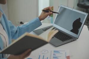 Charming Young asian businesswoman sitting on laptop computer in the office, making report calculating balance Internal Revenue Service checking document. photo