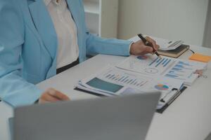 Charming Young asian businesswoman sitting on laptop computer in the office, making report calculating balance Internal Revenue Service checking document. photo