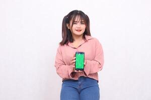 Beautiful happy asian woman in her 20s wearing casual shirt holding green screen cellphone while smiling spoiled on white background studio portrait for banner ad, banner, billboard photo