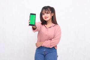 Beautiful happy asian woman in her 20s wearing casual shirt holding cell phone green screen while smiling looking at camera on white background studio portrait for banner ad, banner, billboard photo