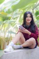 portrait of beautiful sexy asian woman exploring cafe outdoors. smiling girl typing on cellphone looking at camera photo