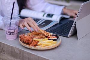 oficina hermosa asiático mujer en al aire libre cafetería. sonriente niña comiendo mientras haciendo trabajo para contenido o publicidad foto