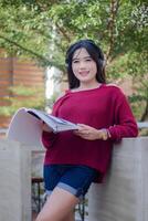 portrait of beautiful sexy asian woman exploring cafe outdoors. focused girl reading book and listening to music looking at camera for content or promo photo