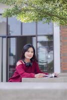 portrait of beautiful sexy asian woman exploring cafe outdoors. girl sitting relaxed smiling reading a book looking at camera for content or promo photo