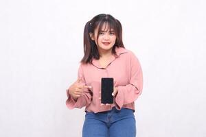 Beautiful happy asian woman in her 20s wearing casual shirt holding cell phone green screen pointing gadget from side on white background studio portrait for banner ad, banner, billboard photo