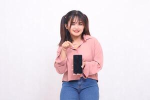 Beautiful happy asian indonesia woman in her 20s wearing casual shirt holding cellphone green screen pointing gadget on white background studio portrait for banner ad, banner, billboard photo