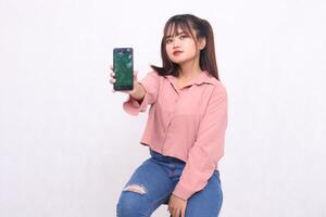Beautiful happy asian woman in her 20s wearing casual shirt holding cellphone greenscreen looking at camera on white color background studio portrait for banner ad, banner, billboard photo