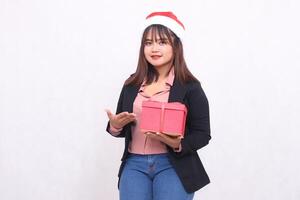 Beautiful Asian girl in cheerful suit with Santa Claus hat posing with Christmas gift box gift and hand presenting gift on white background for promotion, advertising, banner, billboard photo