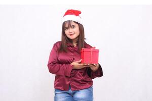Photo portrait of beautiful smiling Asian girl in her 20s carrying boxed gifts at Christmas Santa Claus hat modern shiny red shirt outfit seen on white background for promotion and advertising