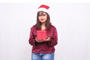 Photo portrait of beautiful Asian girl in her 20s carrying boxed gifts in Christmas Santa Claus hat modern shiny red shirt outfit seen on white background for promotion and advertising