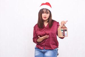 beautiful young woman southeast asia innocent smile introducing gift hamper at christmas wearing santa claus hat modern red shirt outfit white background for promotion and advertising photo
