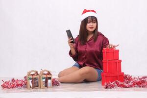 hermosa joven Sureste asiático niña comprobación pedidos siguiente a 3 regalo cajas de cestas a Navidad vistiendo Papa Noel venda y rojo camisa en blanco antecedentes para promoción y publicidad foto