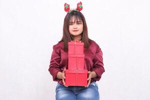 Beautiful young woman from Southeast Asia smiles while carrying 3 boxes of gifts at Christmas wearing a Santa Claus headband and a modern red shirt on a white background for promotion and advertising photo