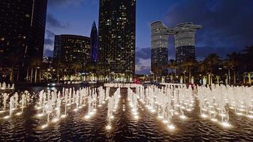 nattetid fontän visa i urban dubai miljö, fängslande nattetid se av en dynamisk fontän visa omgiven förbi upplyst skyskrapor i dubai. video