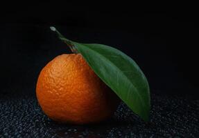 Ripe juicy tangerine on a black background with water drops. photo