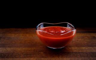 Ketchup in a glass cup on a wooden board. photo