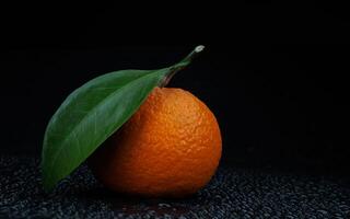 Ripe juicy tangerine on a black background with water drops. photo