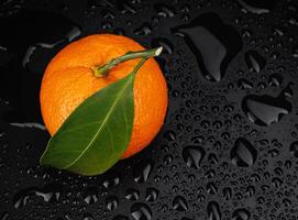 Ripe juicy tangerine on a black background with water drops. photo