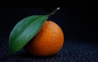 Ripe juicy tangerine on a black background with water drops. photo